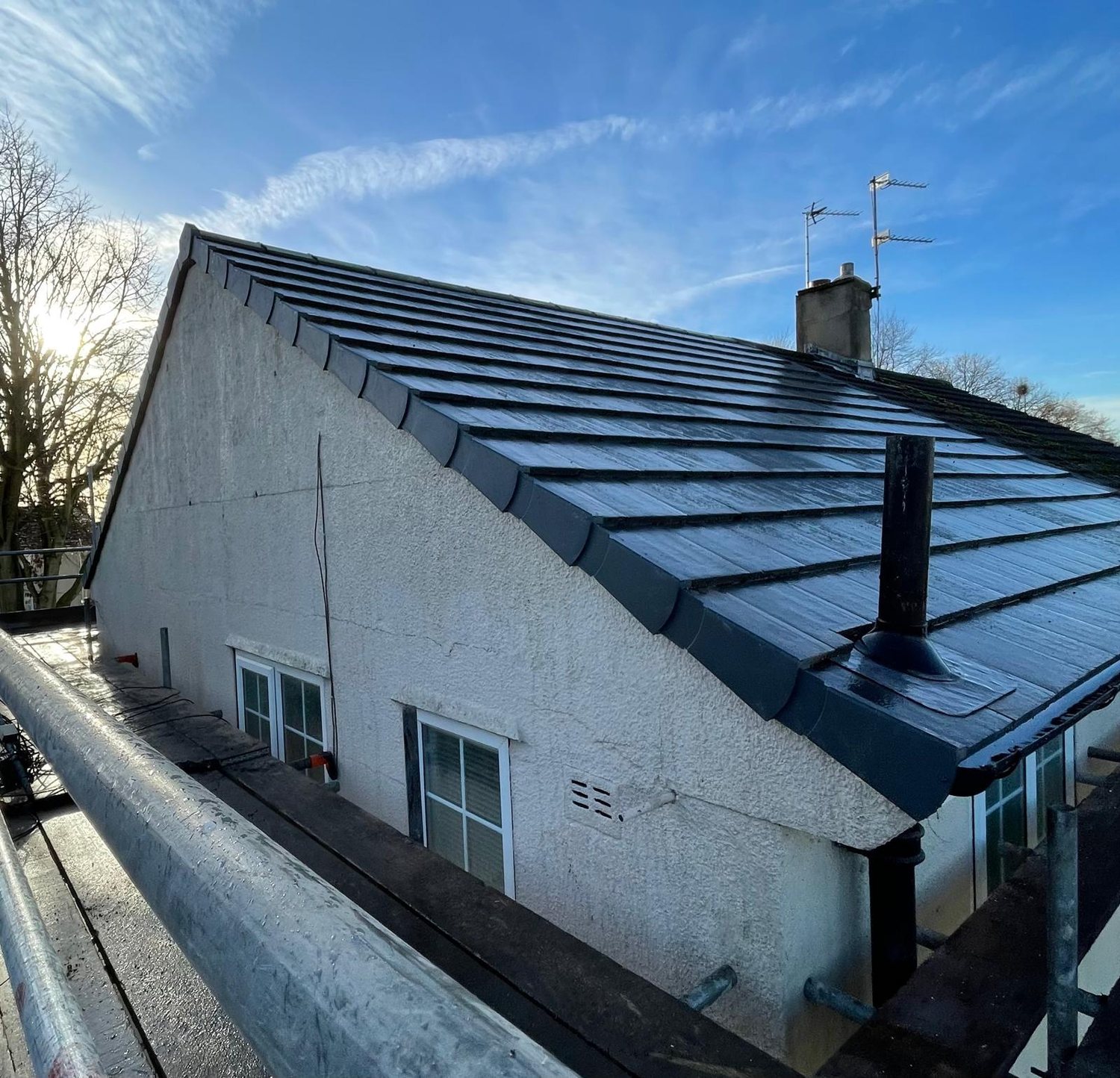 Completed re-roof in dark grey tiles with new ridge, under a blue sky